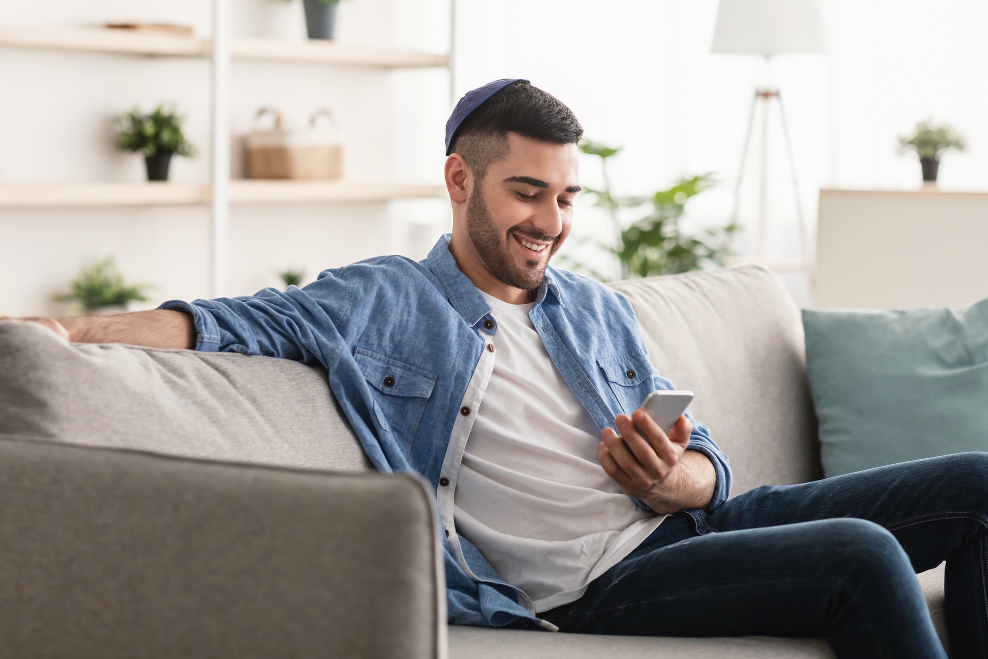 Closeup of smiling jewish man using smartphone at home